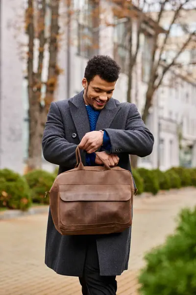 A stylish man looks cheerful while inspecting his brown bag on a pleasant day outdoors — Stock Photo