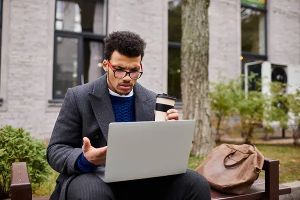 A handsome man enjoys his coffee while working intently on his laptop outdoors. — Stock Photo