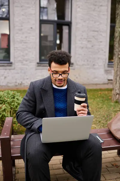 Focused man with glasses types on his laptop, sipping coffee in a tranquil park environment. — Stock Photo