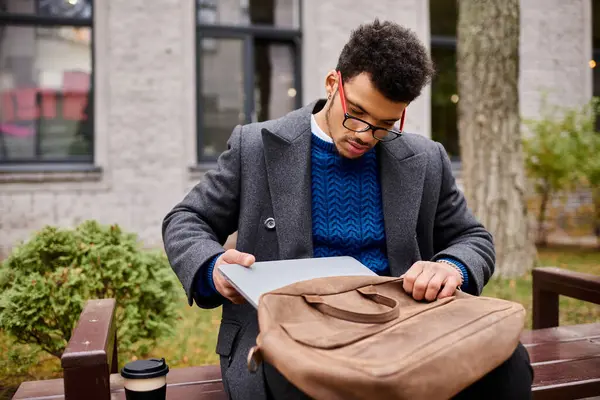 Stylish individual checks his laptop while seated on a wooden bench in a vibrant park. — Stock Photo