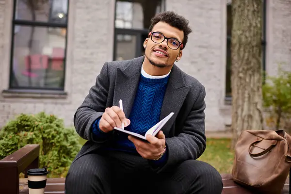 A handsome man sits comfortably writing in his notebook, surrounded by nature and warmth. — Stock Photo