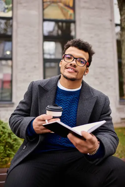 Un individuo elegante si siede comodamente su una panchina, assaporando una bevanda e leggendo un libro. — Foto stock