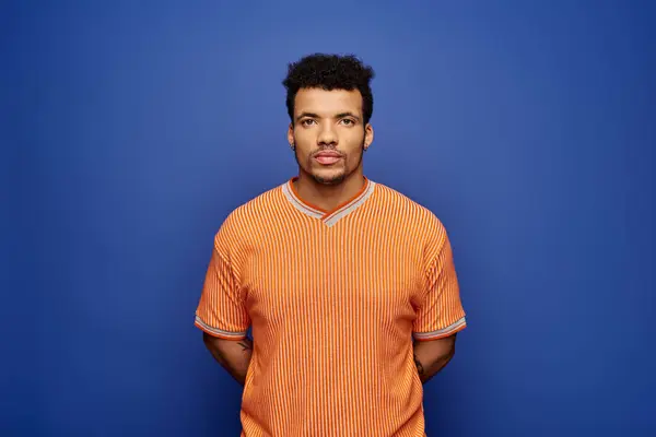 Confident individual with distinct style poses against a bold blue wall in an orange outfit. — Stock Photo