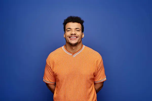 A cheerful man dressed in an orange shirt smiles brightly against a bold blue backdrop. — Stock Photo