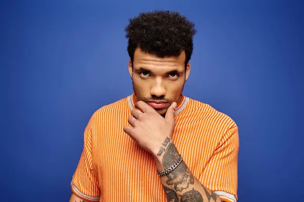 A stylish man with curly hair confidently poses against a bright blue backdrop. — Stock Photo