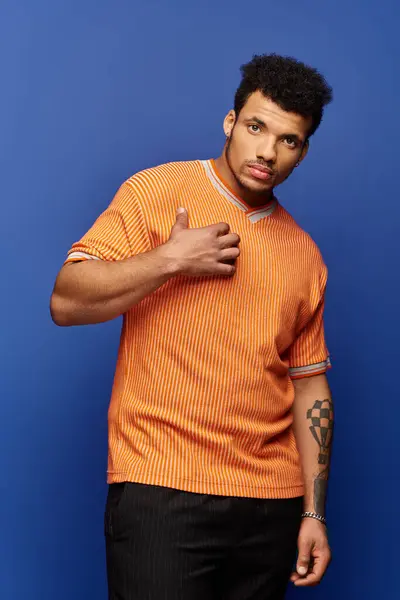 A handsome man stands confidently, gesturing with his hand while wearing an orange shirt. — Stock Photo