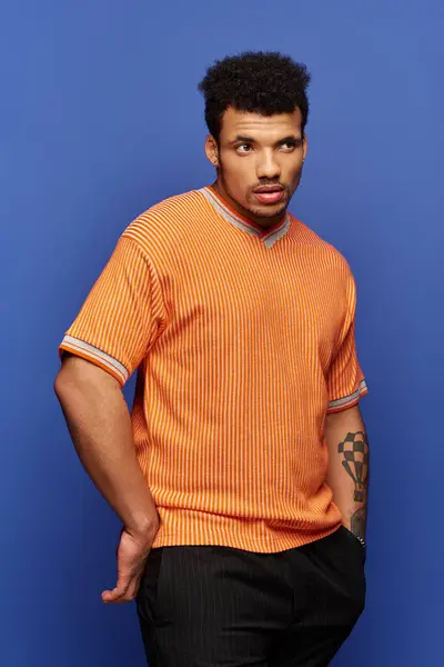 A striking man stands confidently with a unique hairstyle, wearing a bright orange shirt. — Stock Photo