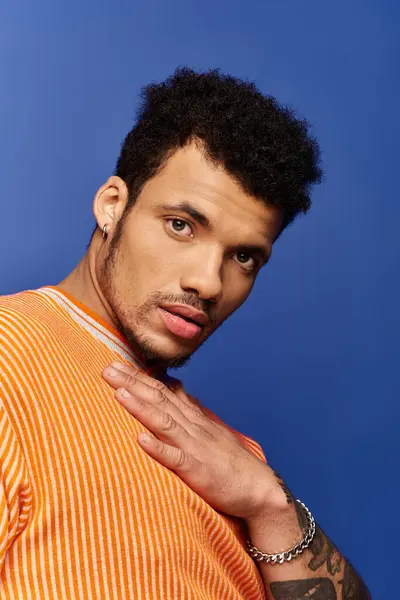 A man in an orange striped shirt exudes charisma against a bright blue backdrop. — Stock Photo