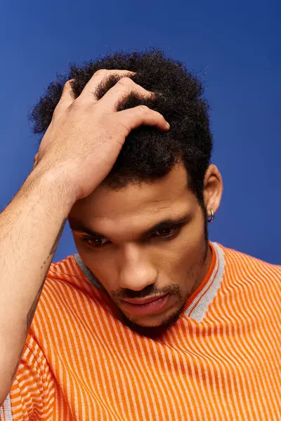 A handsome man in an orange striped shirt ponders deeply while posing with a blue background. — Stock Photo