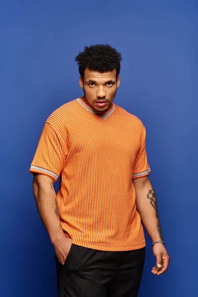A handsome young man stands with a serious expression, showcasing his stylish orange shirt. — Stock Photo