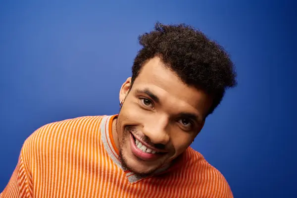 A man with a warm smile wears a striped shirt in front of a vivid blue backdrop. — Stock Photo