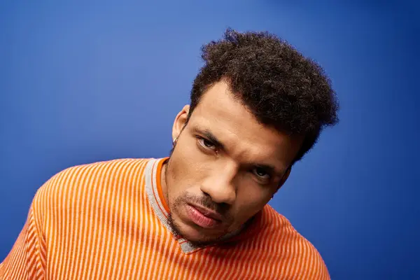 Confident man in a bold orange top poses intensely against a blue backdrop. — Stock Photo