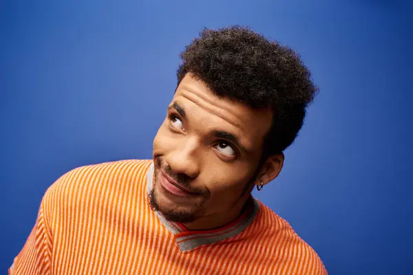 A stylish man with curly hair looks thoughtfully upwards against a bright blue backdrop. — Stock Photo