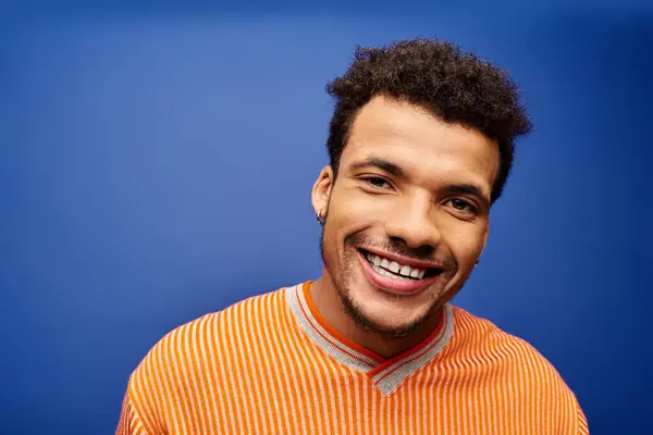 A charming man wearing an orange striped shirt shares a warm smile, showcasing his charisma. — Stock Photo