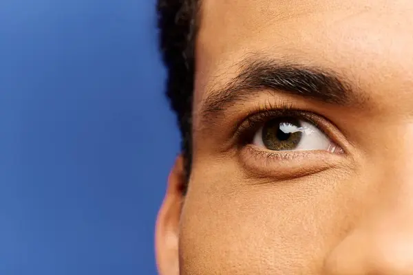 Ein gutaussehender Mann blickt nachdenklich mit auffallend grünen Augen, umrahmt von einem leuchtend blauen Hintergrund. — Stockfoto
