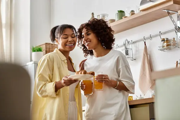 Two young women share laughter and breakfast in their modern apartment during a sunny morning. — Stock Photo
