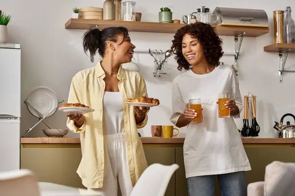Due giovani donne gustare la colazione insieme, condividendo sorrisi e risate in un accogliente appartamento. — Foto stock