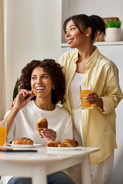 Two young women share a joyful breakfast in their stylish apartment, savoring pastries and drinks. — Stock Photo