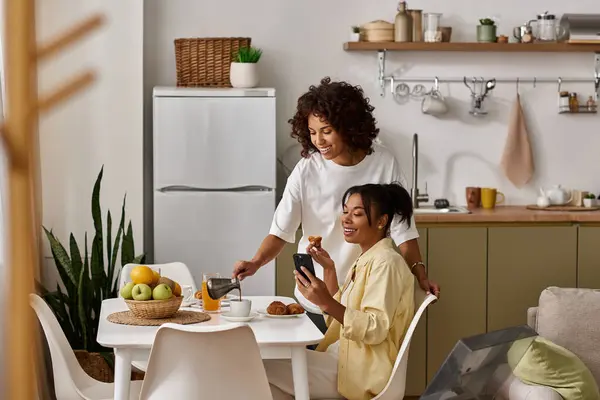 Two women share a joyful breakfast moment, surrounded by modern decor and love. — Stock Photo