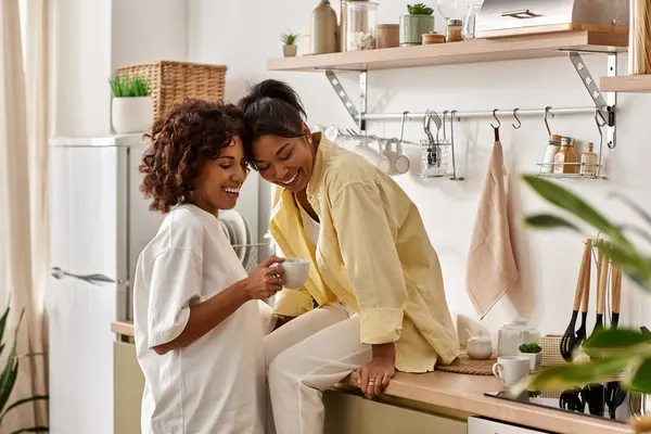 Two young women share laughter and love while relaxing in their stylish kitchen. — Stock Photo