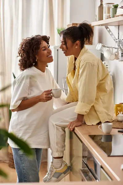 A young lesbian couple enjoys a warm moment together in their stylish kitchen while sipping drinks. — Stock Photo