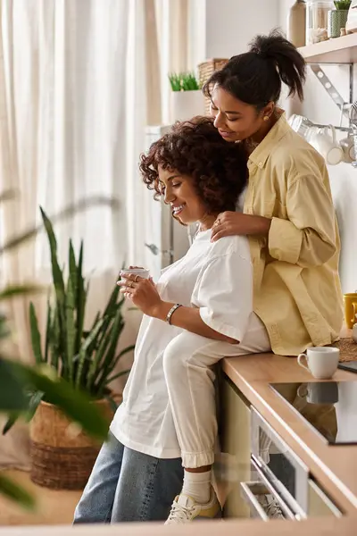 Two young women share a tender moment in their bright apartment, surrounded by plants and warmth. — Stock Photo