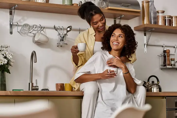 Two young women share a warm moment together in their stylish kitchen, enjoying coffee and laughter. — Stock Photo