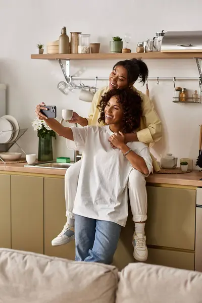 Two young women enjoy a tender moment together in their contemporary apartment while taking selfies. — Stock Photo