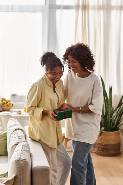 A young African American couple joyfully exchanges a gift in their stylish home, showcasing love. — Stock Photo