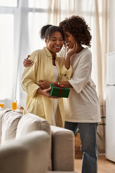 Two young women share a moment of joy and connection while exchanging gifts in their stylish home. — Stock Photo