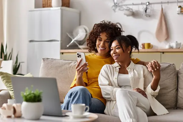 Two women relax together on a sofa, enjoying each others company while using a smartphone. — Stock Photo