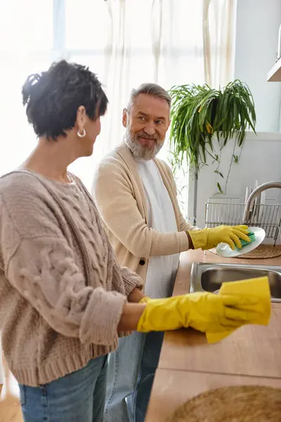 A cheerful couple shares smiles as they clean dishes in a bright, airy kitchen space. — Stock Photo