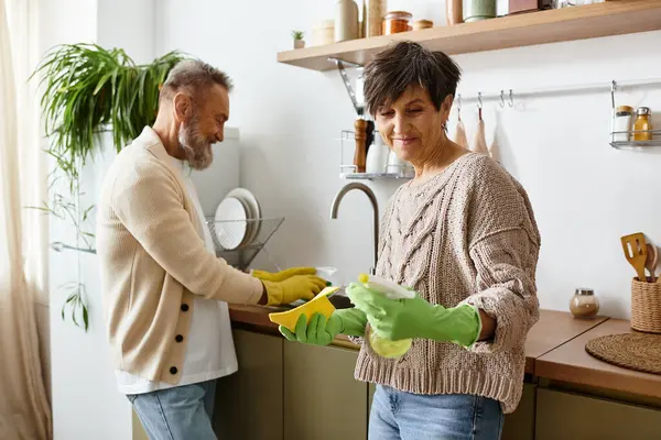 A happy couple smiles while tackling chores together in a bright kitchen. — Stock Photo