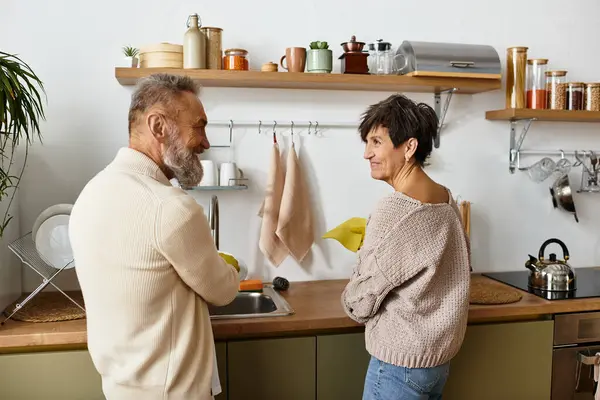 A happy senior couple enjoys washing dishes together in their cozy kitchen. — Stock Photo