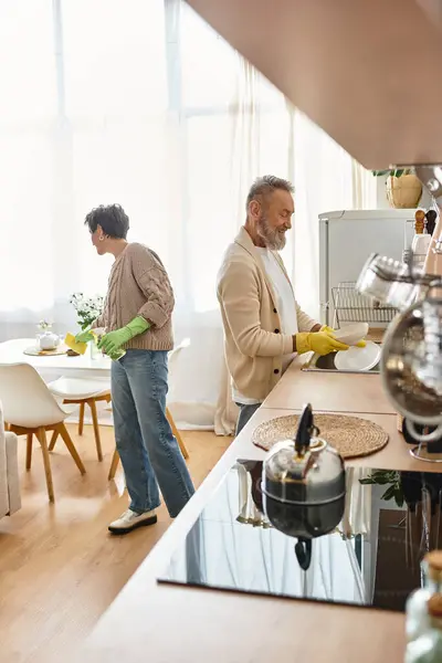 Pareja alegre trabajando en su acogedora cocina, compartiendo momentos mientras limpian juntos. - foto de stock