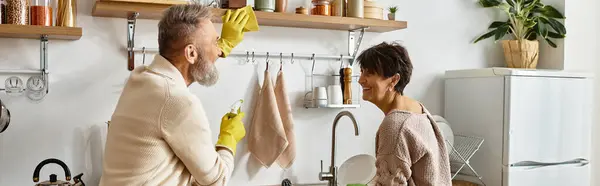 A mature couple enjoys lighthearted fun in their cozy kitchen while preparing a meal. — Stock Photo