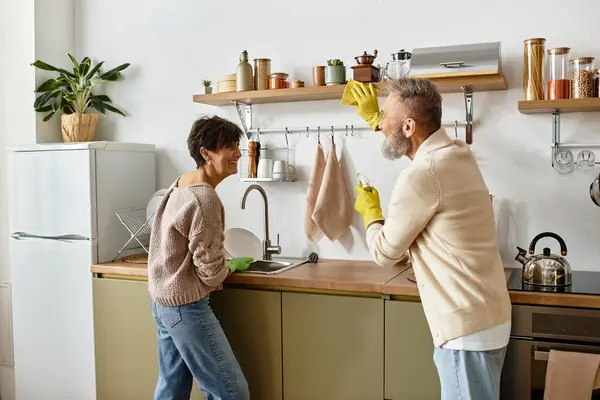 Una feliz pareja se involucra en un momento lúdico mientras lava los platos en su acogedora cocina. - foto de stock