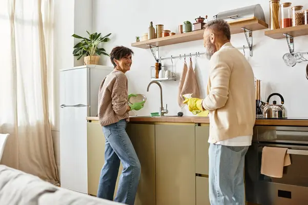 A mature couple cooks together, creating a warm, loving atmosphere in their kitchen. — Stock Photo