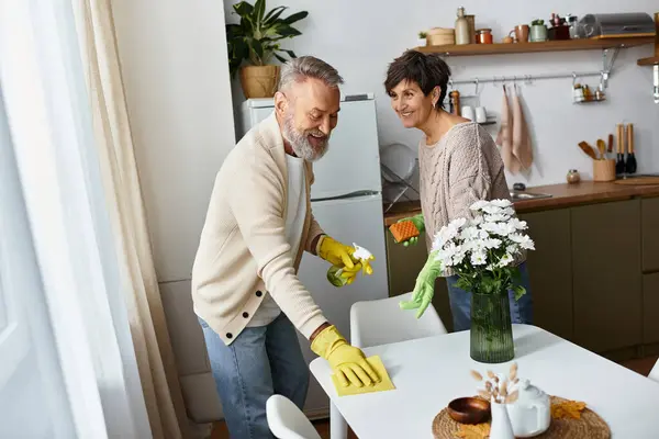 Um casal se envolve em uma limpeza alegre enquanto compartilha sorrisos em seu espaço de cozinha ensolarado. — Fotografia de Stock
