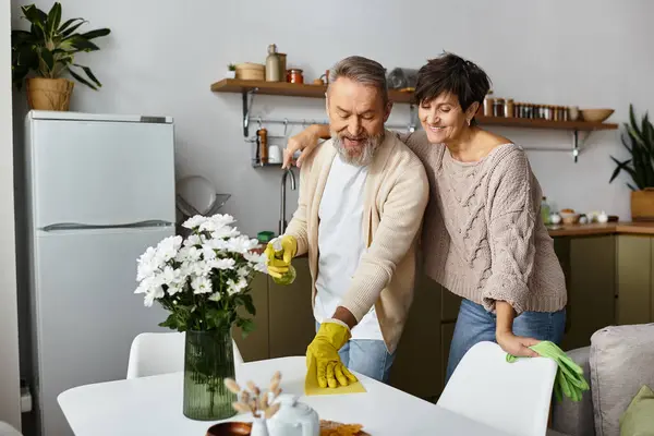 Senior couple shares laughter as they clean their kitchen, creating a joyful atmosphere together. — Stock Photo