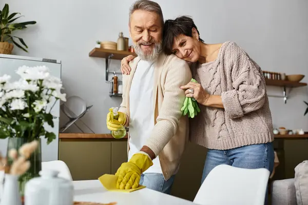 A happy mature couple tidies up their inviting kitchen, sharing warm moments and laughter. — Stock Photo