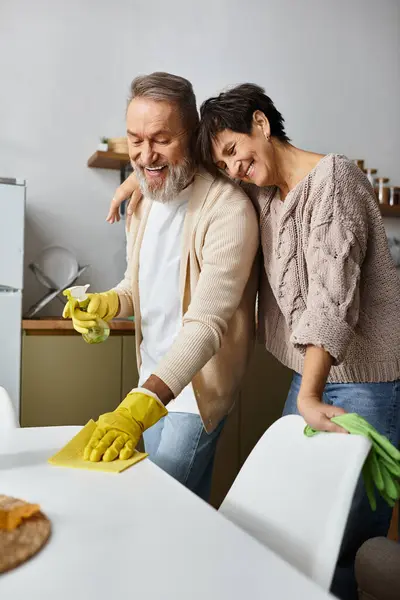A mature couple enjoys cleaning their kitchen, laughing and bonding over shared tasks and smiles. — Stock Photo