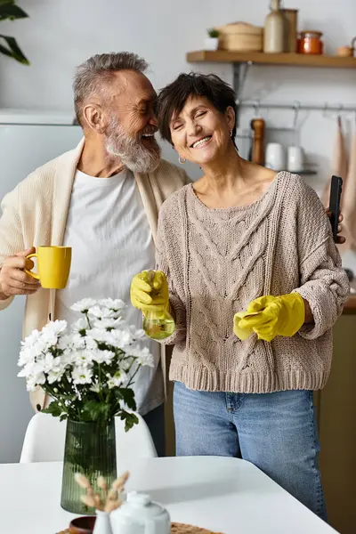 A mature couple happily engages in kitchen chores, radiating love and warmth while laughing. — Stock Photo