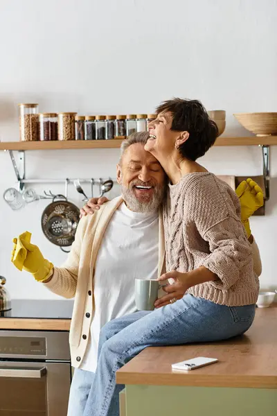 A cheerful senior couple enjoys a playful moment in their kitchen, sipping coffee and laughing. — Stock Photo