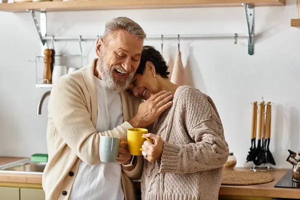 A mature couple embraces warmly while enjoying their coffee in a cheerful kitchen atmosphere. — Stock Photo