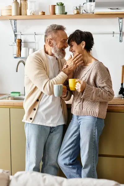 A mature couple shares a tender moment while holding warm cups in their charming kitchen. — Stock Photo