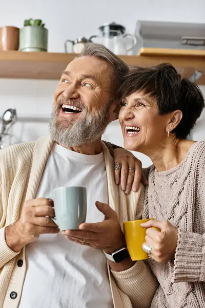 A mature couple enjoys laughter and warm drinks in their cozy kitchen, creating memories. — Stock Photo