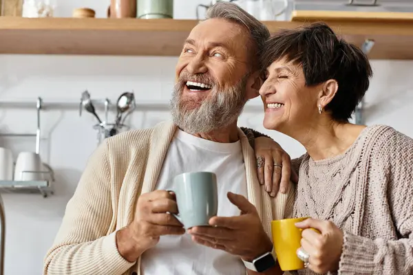 Couple sharing laughter and joy over warm drinks in their cozy kitchen setting at home. — Stock Photo