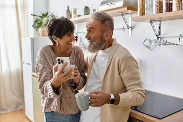 Um casal maduro desfruta de um momento delicioso juntos enquanto compartilha uma risada sobre um smartphone. — Fotografia de Stock