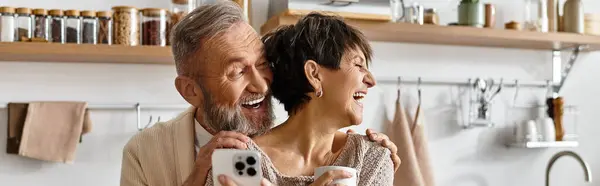 Pareja madura comparte la risa y el calor mientras disfrutan de las bebidas juntos en su elegante cocina. - foto de stock